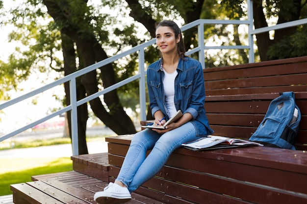 Image of amazing young beautiful woman sitting outdoors writing notes in notebook.