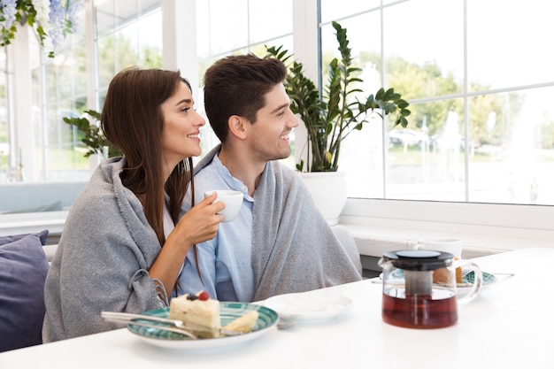 Image of amazing young loving couple sitting in cafe eat desserts and drinking tea.