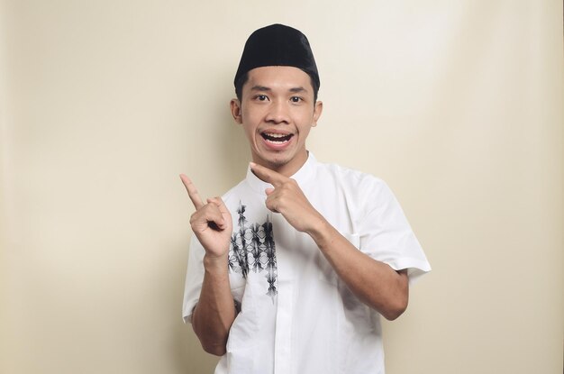 驚きを表現し、人差し指を脇に向けて面白い若いアジアのイスラム教徒の男性の画像