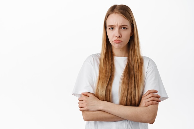 Image of angry offended blond girl sulking and frowning upset about unfair thing cross arms on chest and pouting disappointed standing over white background