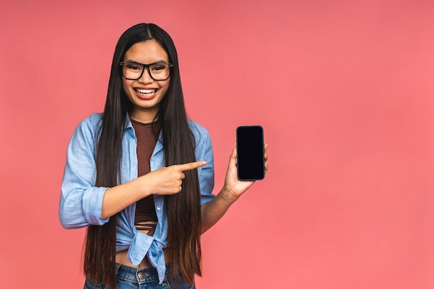 Foto immagine di una donna d'affari asiatica che mostra l'interfaccia dell'app sullo schermo dello smartphone e il segno ok che consiglia l'applicazione sul telefono cellulare isolato su sfondo rosa
