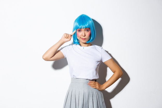 Image of asian girl in blue wig looking skeptical, pointing finger at head, standing.