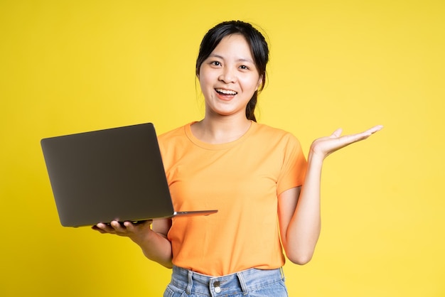 Image of asian girl holding laptop and isolated on yellow background