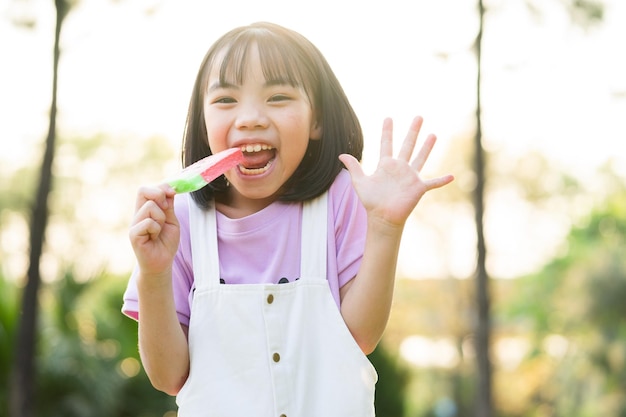 Изображение азиатской маленькой девочки, поедающей мороженое в парке