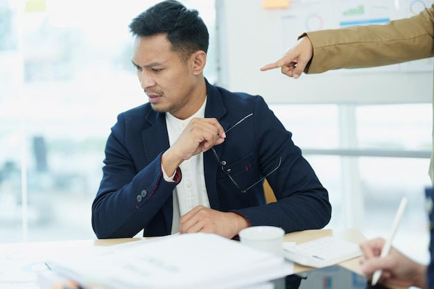 An image of an Asian male employee looking worried and sad about being scolded by his boss for failing to meet sales targets concept of disappointment and failure in his career