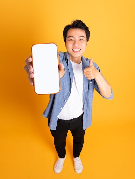 Image of asian man holding phone isolated on yellow background