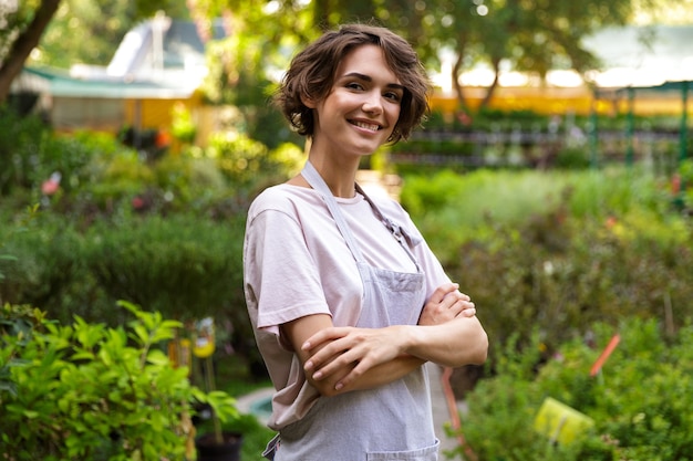 温室の花の植物の上に立っている魅力的なかわいい女性の庭師の画像