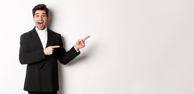 Image of attractive smiling guy dressed for new year party pointing fingers right and showing advert