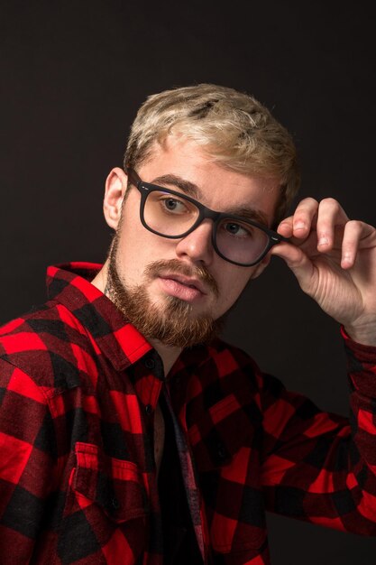 Foto immagine di un attraente giovane hipster barbuto con gli occhiali vestito in camicia in una gabbia isolata su sfondo nero.