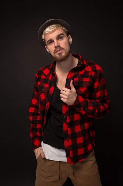 Image of attractive young bearded hipster man wearing hat dressed in shirt in a cage isolated over black background.