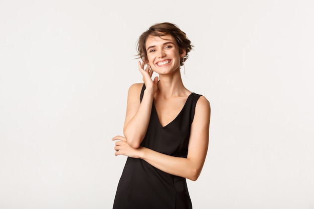 Image of attractive young woman in elegant black dress, smiling happy, standing over white.