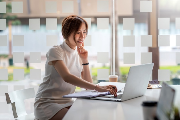 Изображение красивой азиатской женщины, работающей на планшете и документах в современном офисе.