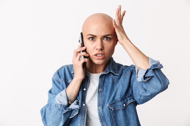 Image of a beautiful displeased angry bald woman posing isolated, talking by mobile phone.