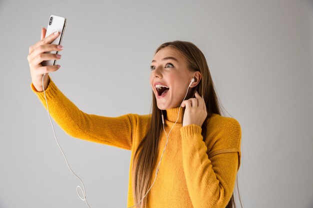 Image of a beautiful excited happy young woman isolated over grey wall using mobile phone talking.