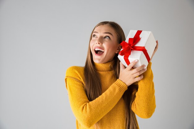 Image of a beautiful shocked happy young woman isolated over grey wall holding gift present box.