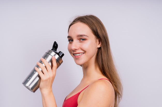 孤立した屋内で水を飲みながらポーズをとっている美しい強い幸せな陽気な若いスポーツの女性の画像