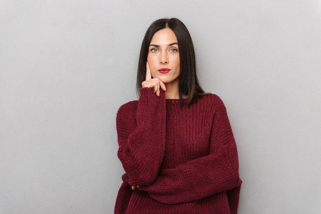 Изображение красивой мышления молодой женщины, одетой в бордовый свитер, изолированные на белом фоне.