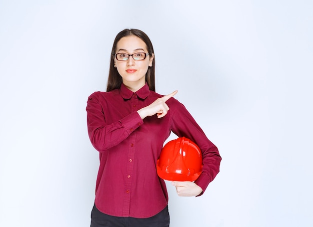 Image of beautiful woman in glasses holding crash helmet and pointing finger aside. 