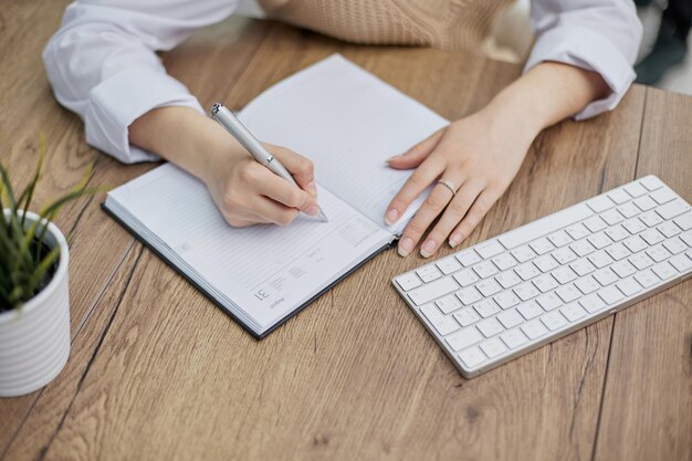 Image beautiful woman writing down notes while sitting at table in office