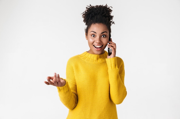 Immagine di una donna felice emotiva emozionante giovane e bella africana in posa sul muro bianco parlando dal telefono cellulare