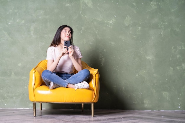 Image of beautiful young Asian woman sitting on yellow armchair