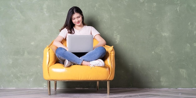 Image of beautiful young Asian woman sitting on yellow armchair