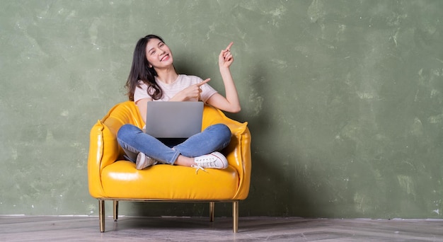 Image of beautiful young Asian woman sitting on yellow armchair