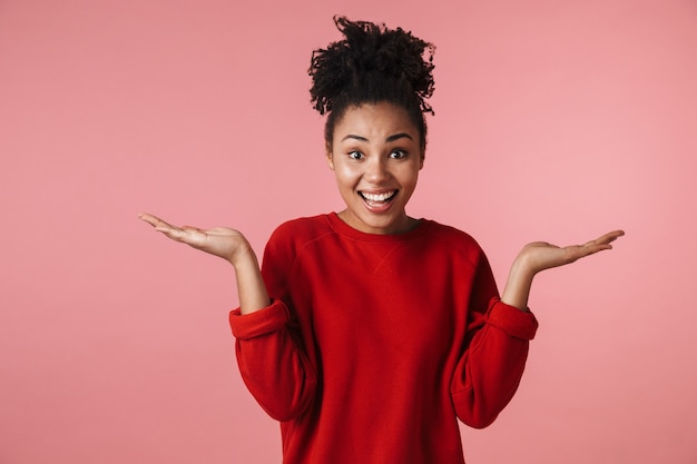 Image of a beautiful young excited happy african woman posing over pink wall showing copyspace.