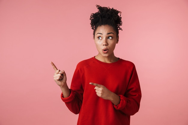 Image of a beautiful young excited happy emotional african woman posing over pink wall pointing.