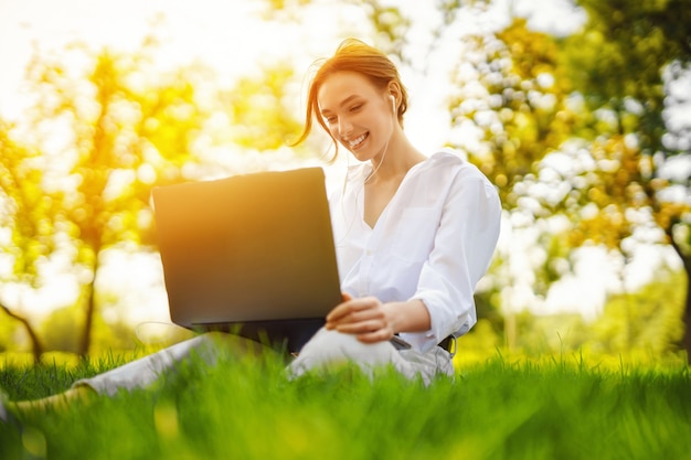 Изображение красивой молодой красивой рыжей женщины в парке на открытом воздухе с помощью портативного компьютера для учебы или работы