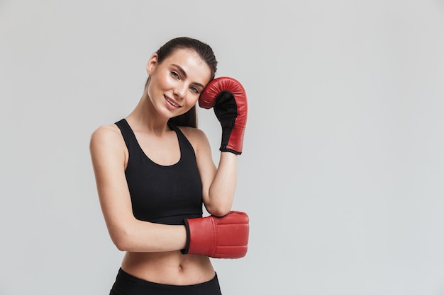 灰色の壁に隔離された美しい若いスポーツフィットネス女性ボクサーの画像は、手袋でエクササイズをします。