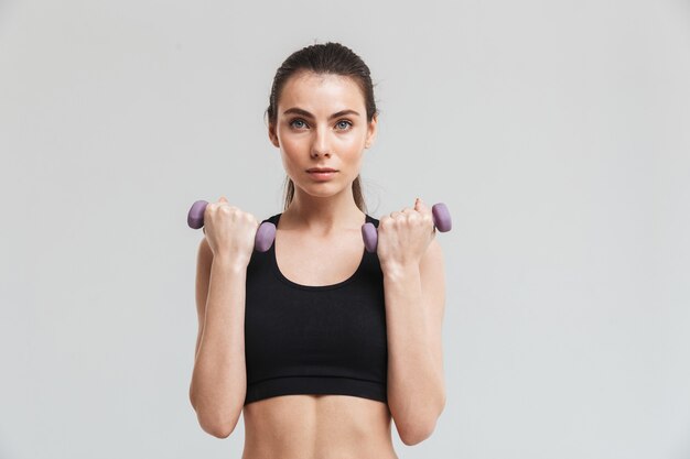 Image of a beautiful young sport fitness woman make exercises with dumbbells isolated over grey wall.