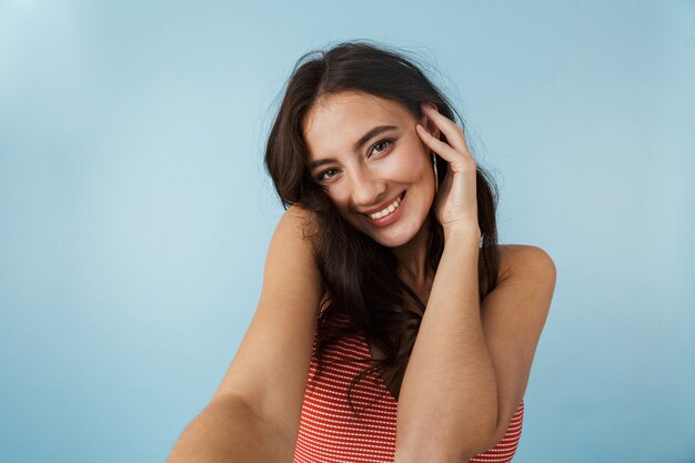 Image of a beautiful young woman posing isolated over blue wall take selfie by camera