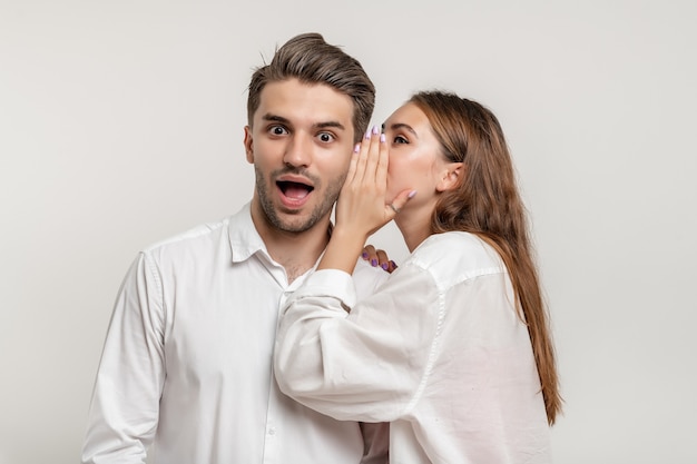 Image of beautiful young woman whispering secret to shocked man in his ear isolated