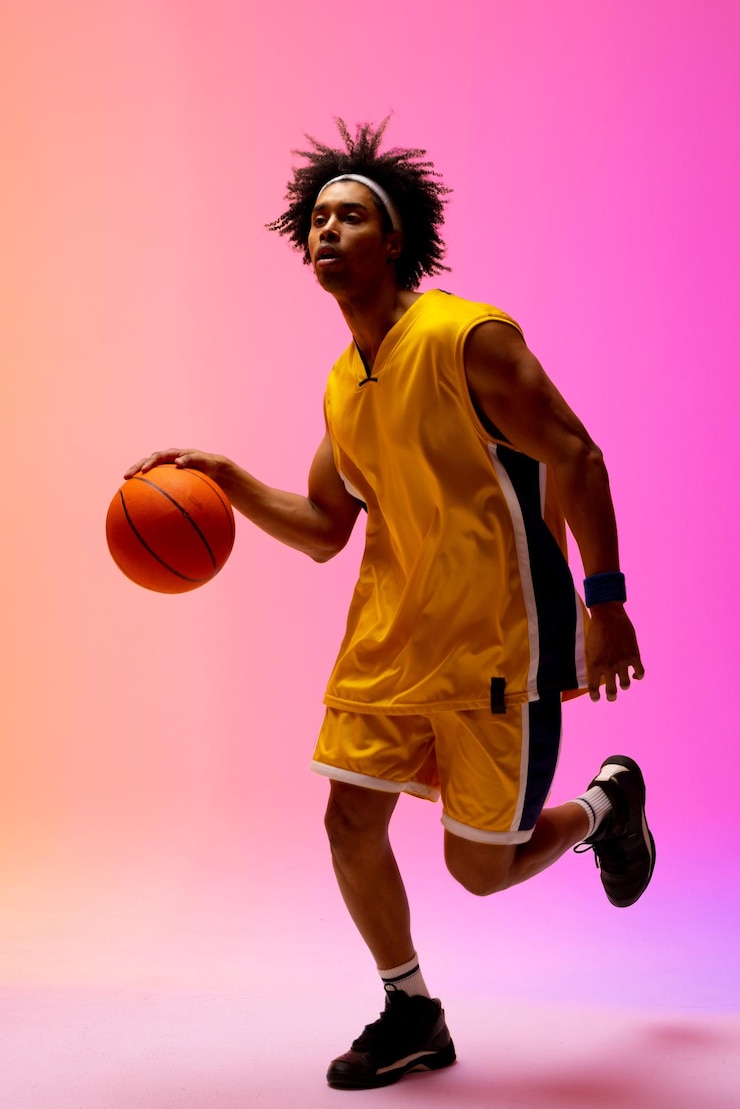 Photo image of biracial basketball player bouncing basketball on pink to orange background. sports and competition concept.