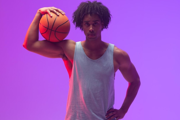 Image of biracial basketball player with basketball on neon purple background. sports and competition concept