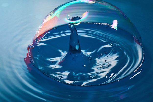 Image of Blue surface and bubble as water drop almost breaks into bubble to collide with another stream of water