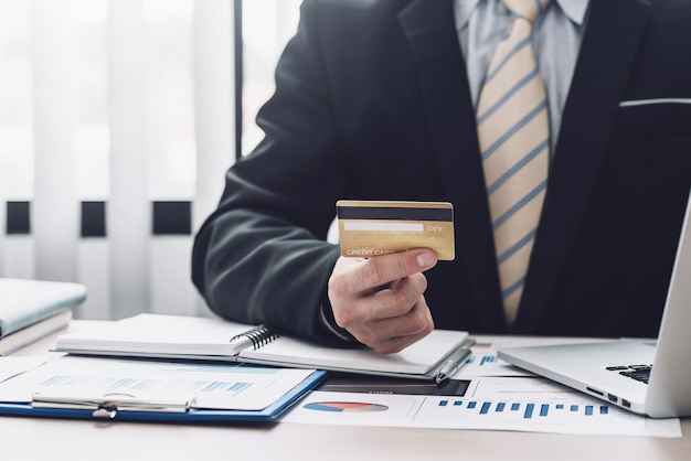 Image of a businessman hand holding a credit card for online shopping using a laptop graph placed at the office.