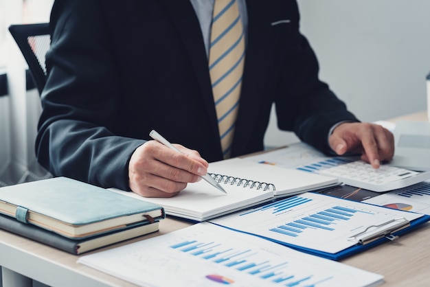 Photo image of businessman hand holding a pen to taking notes ready to use calculator the graph is placed on the office desk. accounting concept.