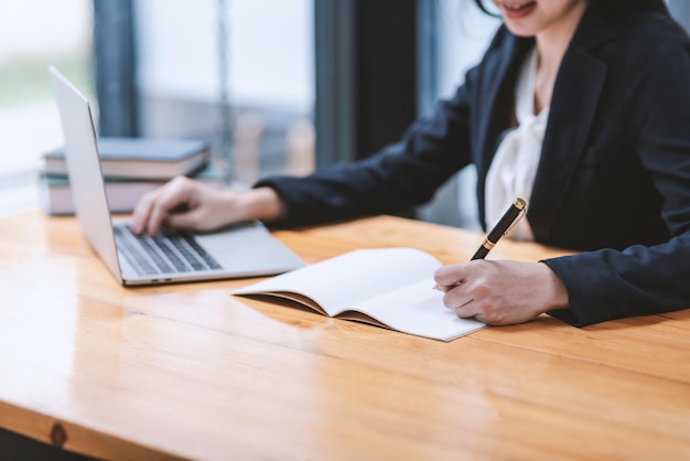 Image of a businesswoman holding a pen to taking notes using a laptop keyboard at the office.