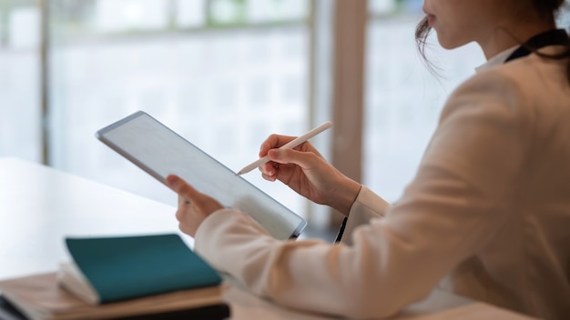 Изображение деловой женщины, сидящей с ручкой и работающей над планшетом в офисе.