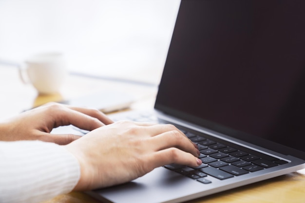 この画像には、ぼやけたオフィスの背景に置かれた洗練されたラップトップのキーボードで入力する女性の手が詳細に捉えられています。
