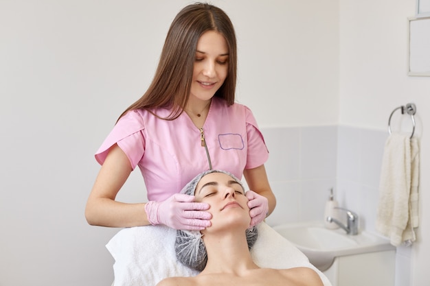 Image of careful positive cosmetologist making anti wrinkle facial massage