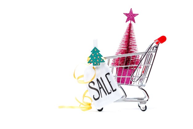 Image of cart with Christmas tree, greeting card, ribbon on empty white surface. Place for text