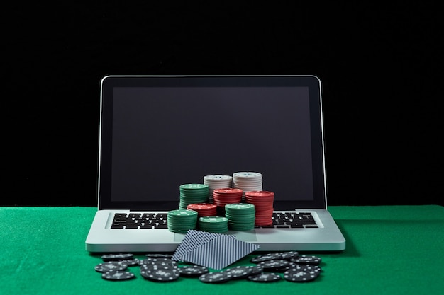 녹색 테이블에 있는 키보드 노트북에 있는 카지노 칩과 카드의 이미지. 온라인 도박, 포커, 가상 카지노에 대한 개념.
