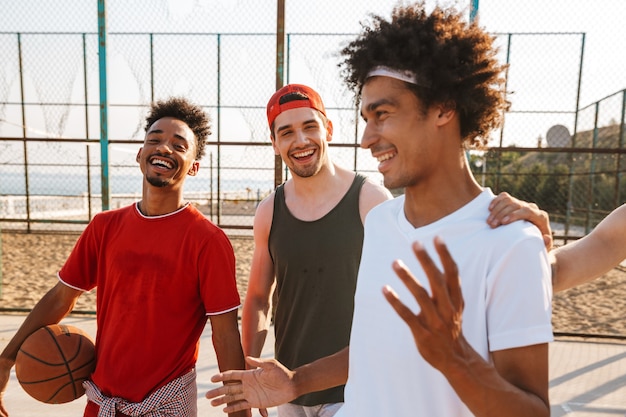 Photo image of caucasian and american men playing basketball at the playground outdoor, during summer sunny day