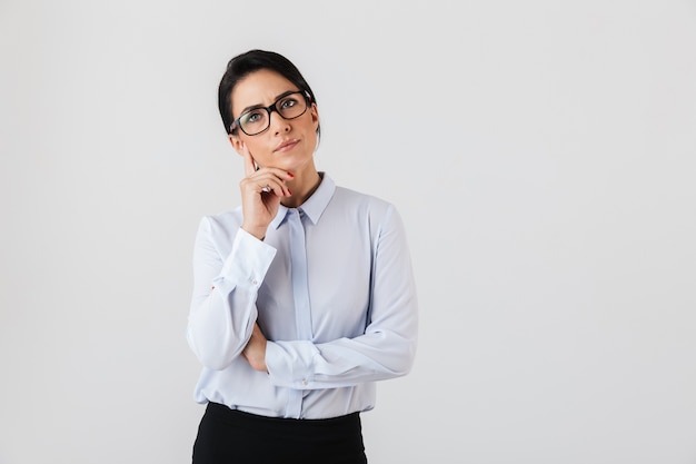 白い壁に隔離されたオフィスに立っている眼鏡をかけている白人秘書の女性の画像