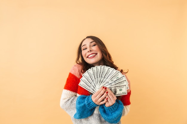 Image of charming woman 20s with long hair smiling and holding fan of money, standing isolated 