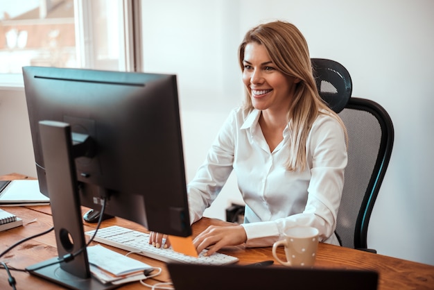 Immagine della donna bionda allegra che lavora al computer.