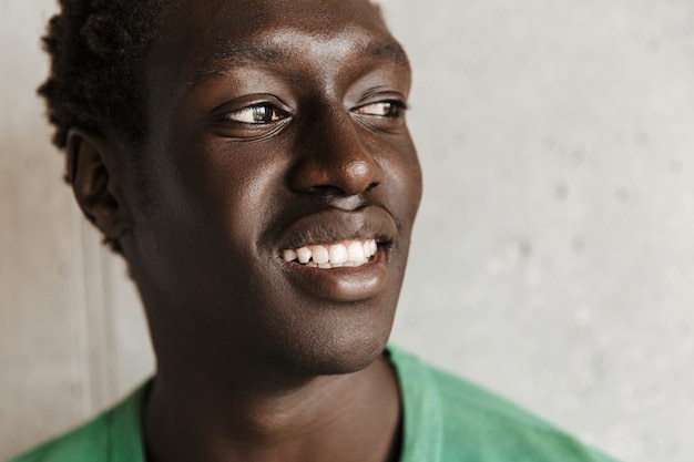 Image of cheerful happy young african american man in casual clothes smiling and looking aside while standing over wall